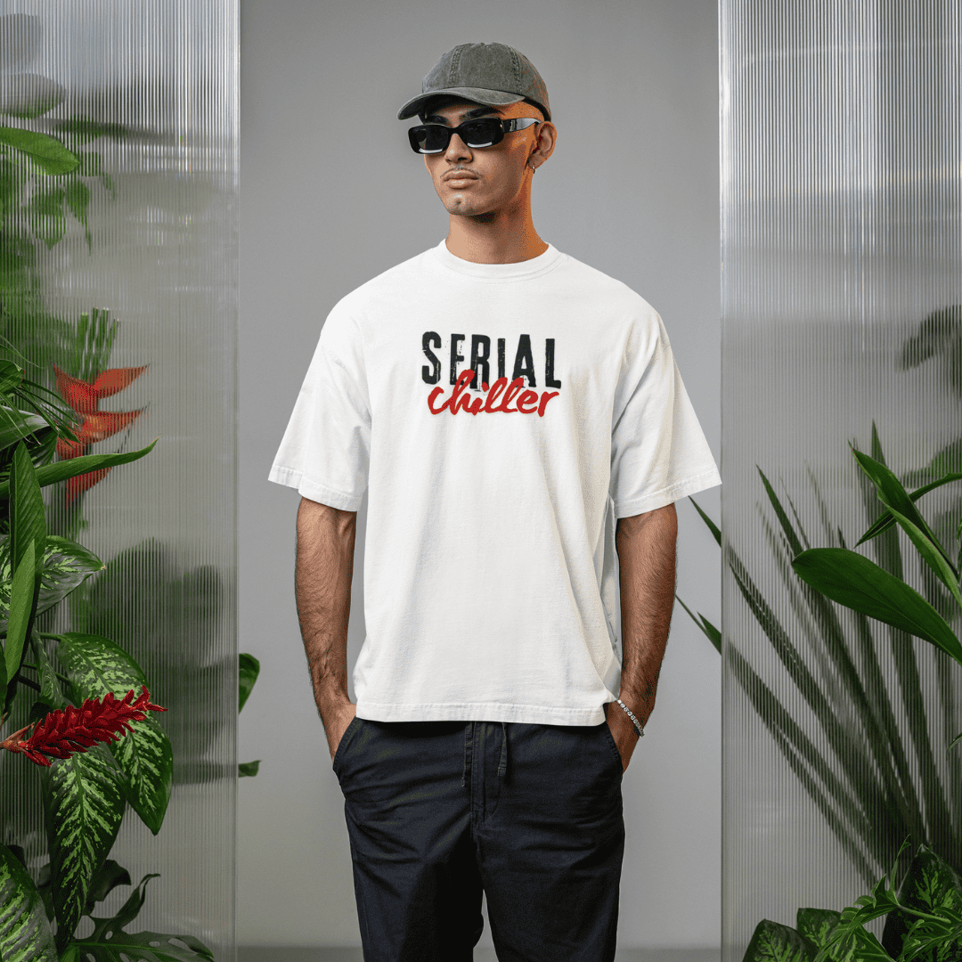 Person wearing a white t-shirt with 'Serial Chiller' text, sunglasses, and cap in a plant-filled room. wordsarmor