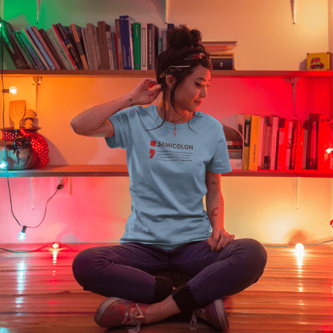 Person sitting on the floor wearing a t-shirt with a visible brand semicolon logo, in a room with colorful lighting. wordsarmor
