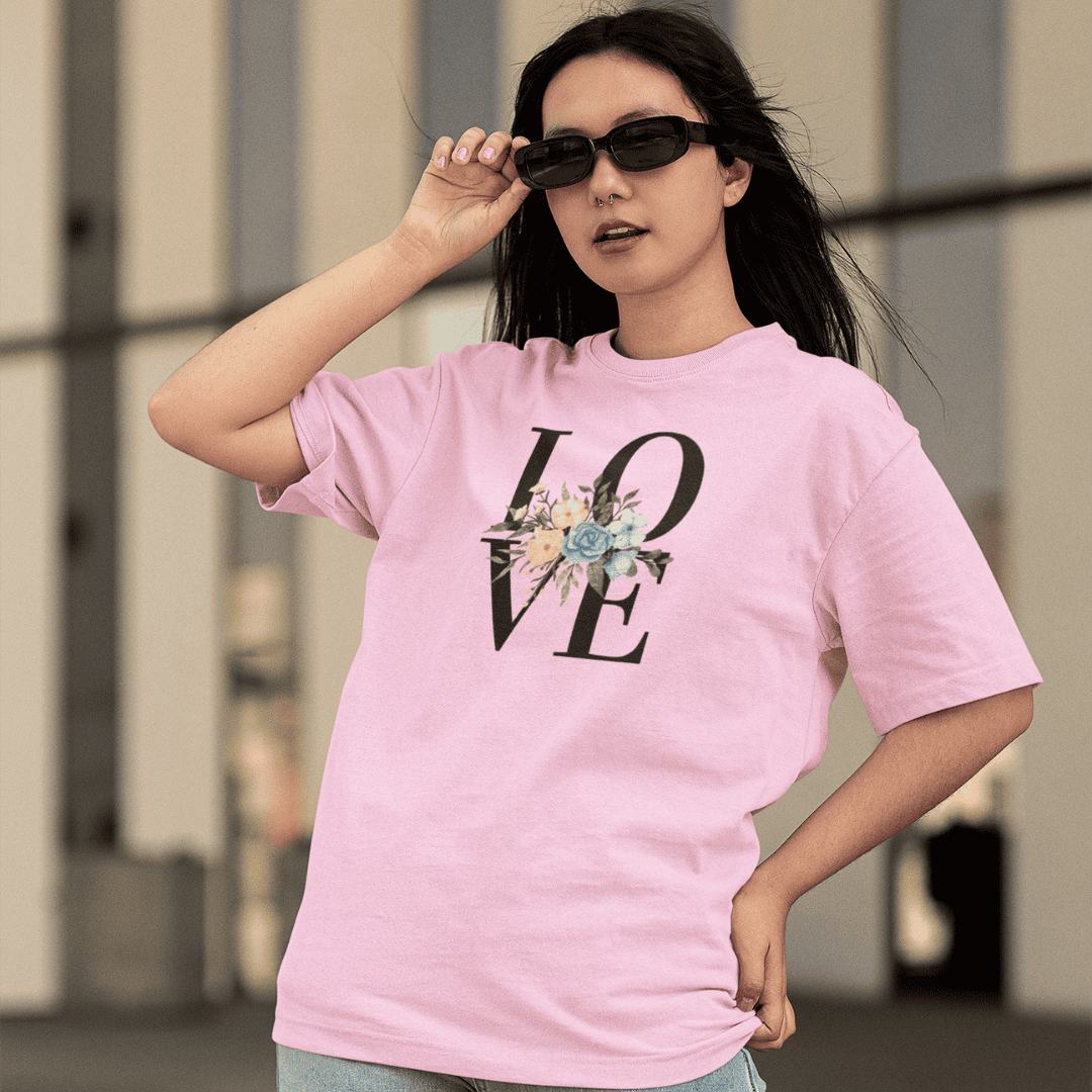Woman wearing a baby pink t-shirt with a floral 'LOVE' design outdoors. wordsarmor