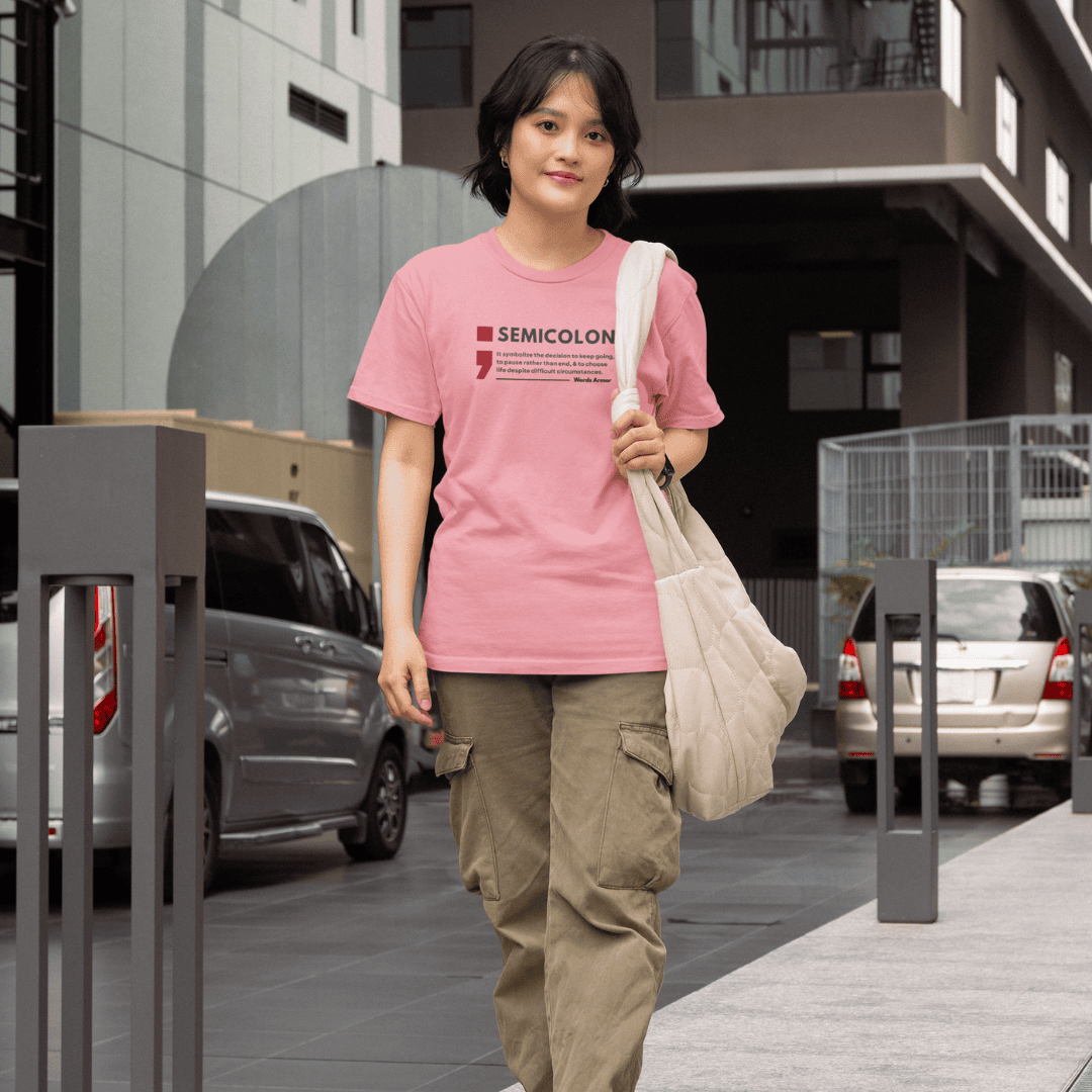 Person wearing a flamingo pink t-shirt with 'SEMICOLON' design on a city street. wordsarmor