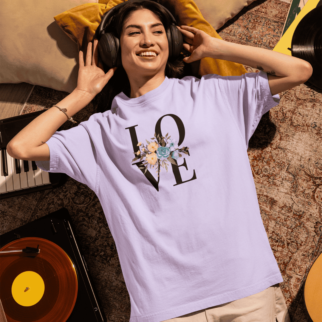 Person wearing a 'LOVE' t-shirt with floral design, lying on a couch with headphones on. wordsarmor