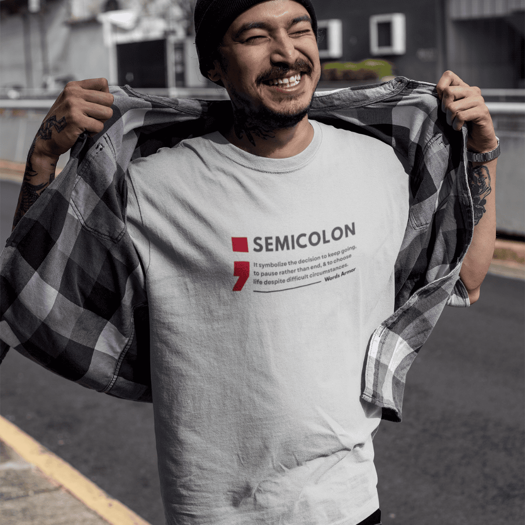 Person wearing a melange grey t-shirt with 'SEMICOLON' design, holding a checkered shirt. wordsarmor