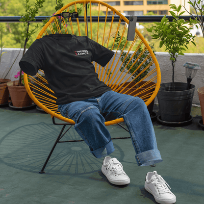 Person wearing a black t-shirt with text, blue jeans, and white sneakers sitting on a yellow chair outdoors. wordsarmor