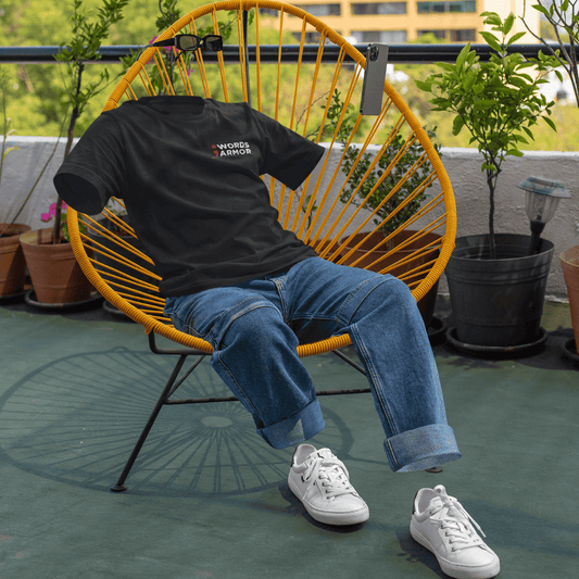 Person wearing a black t-shirt with text, blue jeans, and white sneakers sitting on a yellow chair outdoors. wordsarmor