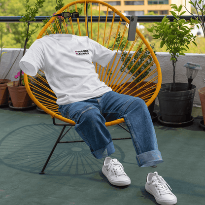 Person wearing a white t-shirt with text and blue jeans sitting on a yellow chair outdoors wordsarmor.