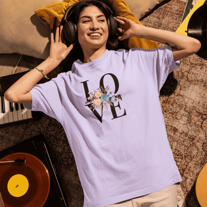 Person wearing a 'LOVE' t-shirt with floral design, lying on a couch with headphones on. wordsarmor